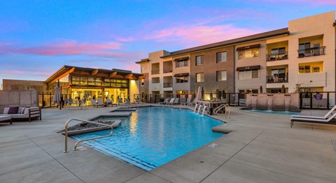 A large swimming pool is surrounded by lounge chairs and umbrellas in a courtyard.