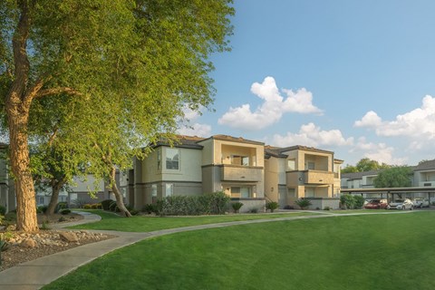 a row of apartment buildings with a green lawn and trees
