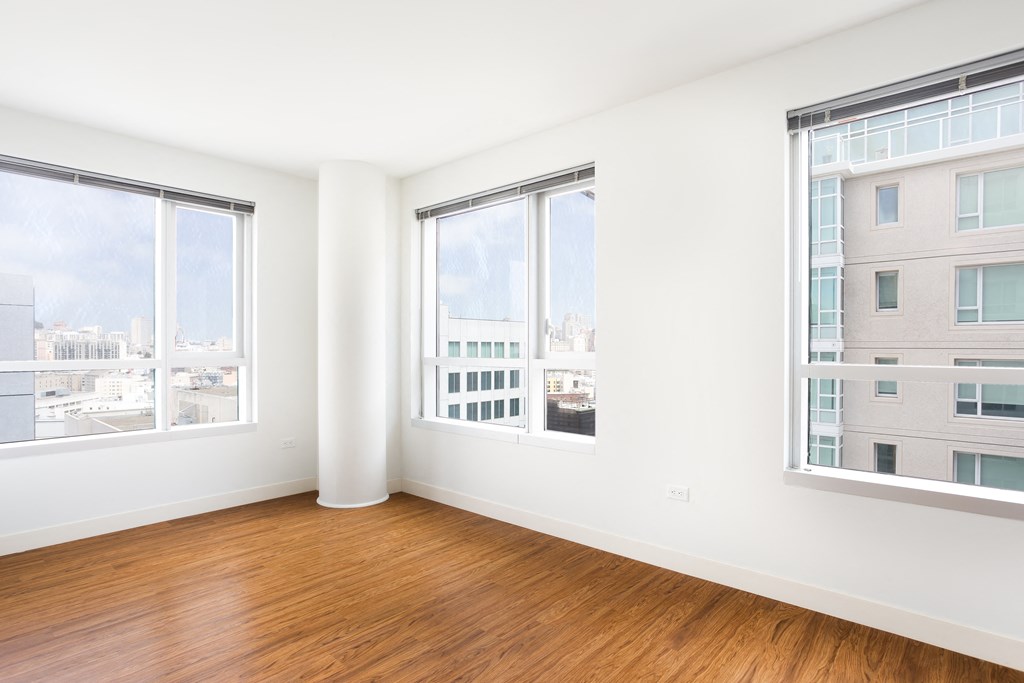 a bedroom with three large windows and a hardwood floor