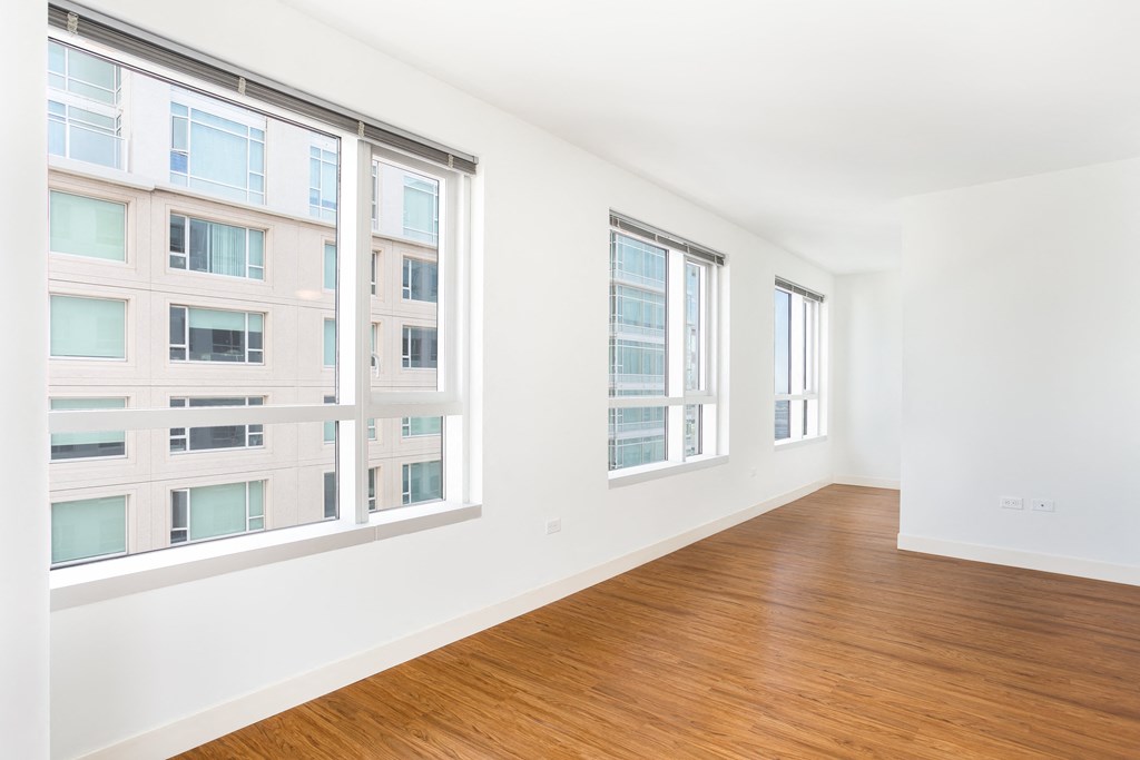 a bedroom with three large windows and a hardwood floor