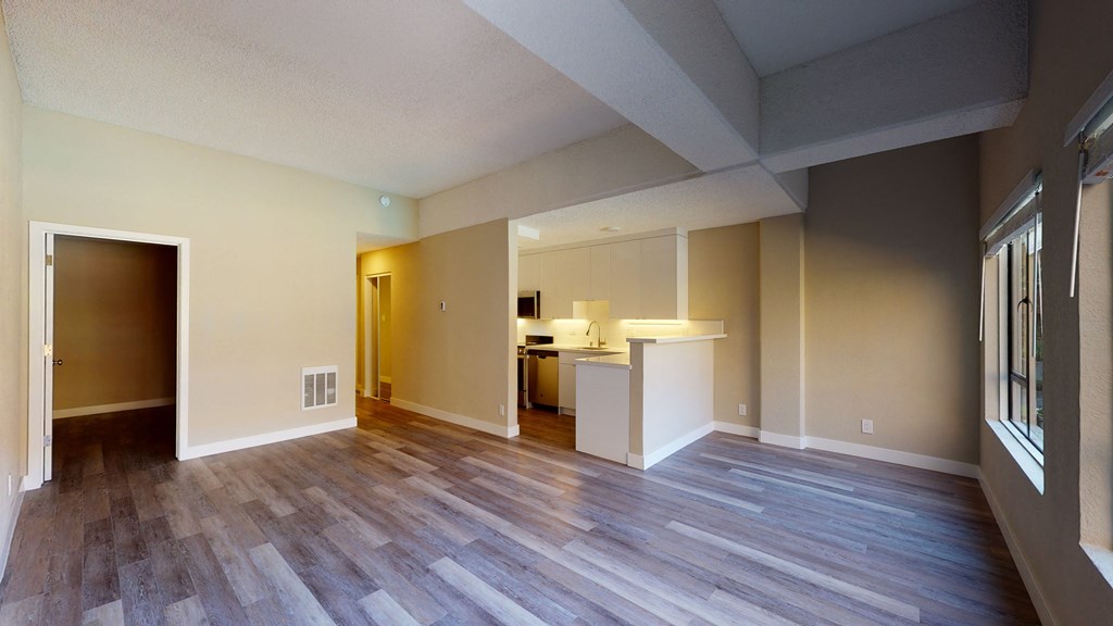 an empty living room with a kitchen in the background