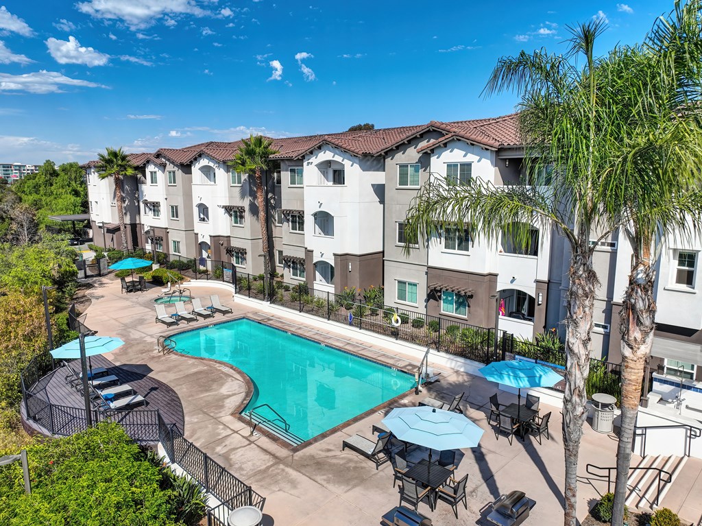 A large swimming pool surrounded by chairs and umbrellas in front of apartment buildings.