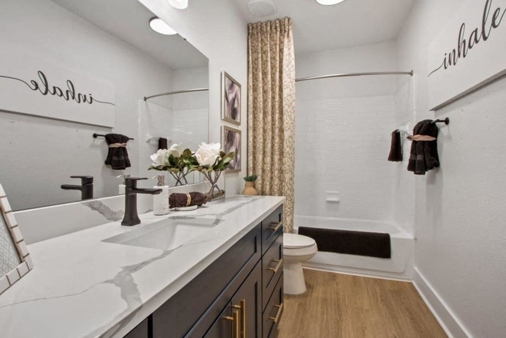 Downtown Savannah, GA, Pet-Friendly Apartments - Adara at Godley Station - Bathroom with Wood-Style Flooring, Large Vanity with Single Sink, Wide Mirror, Cabinet, Light Fixtures, and Bathtub.