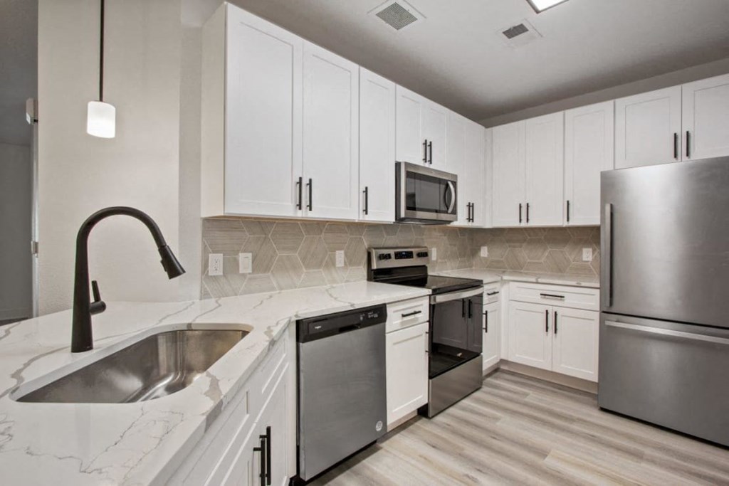 Apartments in Downtown Savannah, GA, with In-Unit Washer and Dryer - Adara at Godley Station - Kitchen with Wood-Style Flooring, White Cabinetry, Pendant Lighting, Dishwasher, Range, Microwave, and Refrigerator.