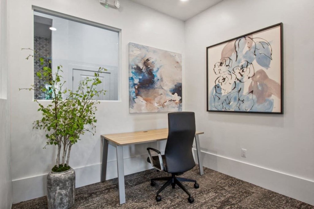 A room with a desk, chair, and two paintings on the wall.