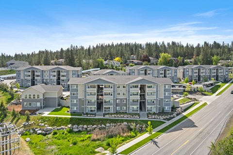 A row of modern apartment buildings are surrounded by trees and grassy areas.