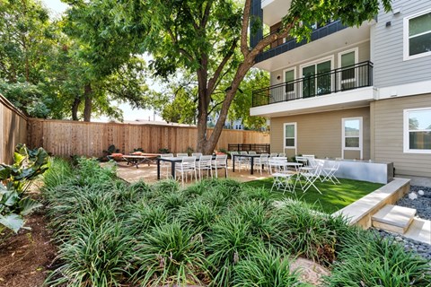 A backyard with a wooden fence and a patio table surrounded by green plants.