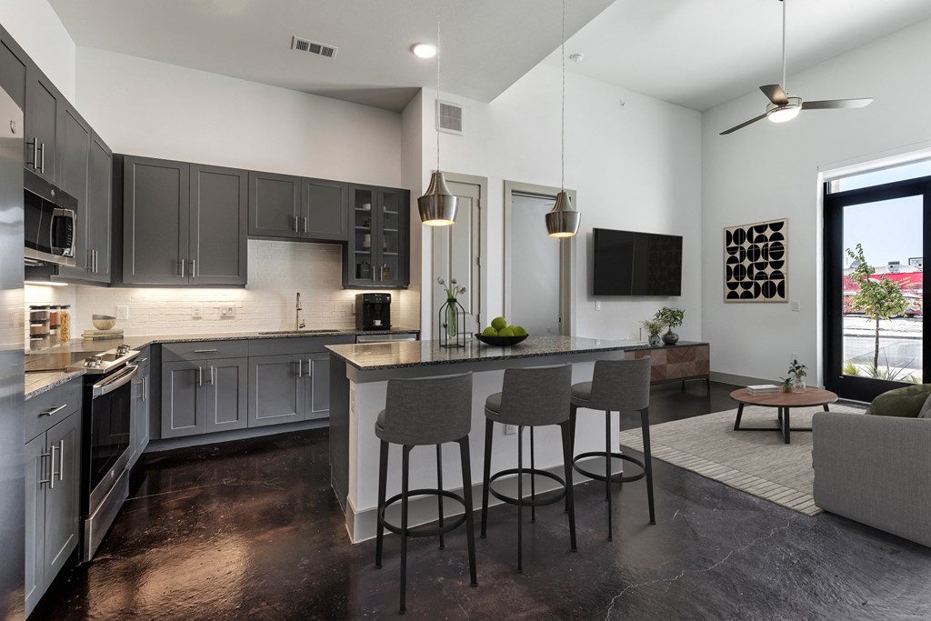 a kitchen and living room with gray cabinets and an island with three stools