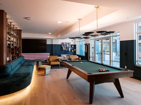 A pool table is in the middle of a room with a bar and a couch.