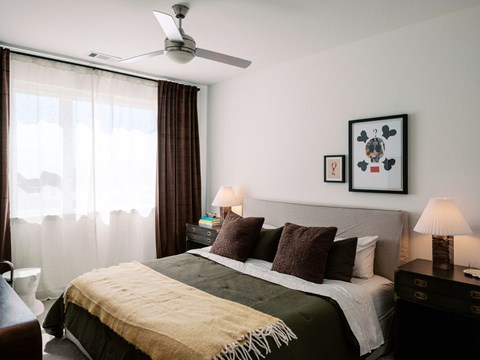 A bedroom with a bed, two lamps, a ceiling fan, and two pictures on the wall.