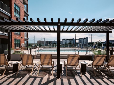 A pool area with chairs and a pergola.