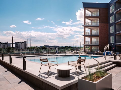 A pool area with chairs and a building in the background.