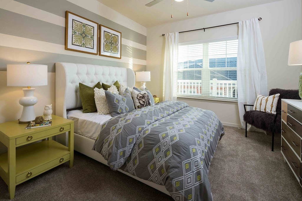 A bedroom with a large bed and a window with white curtains.