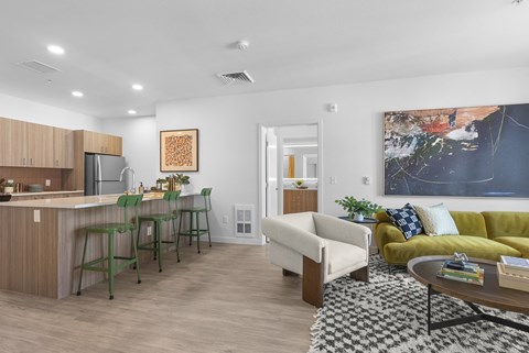 A modern living room with a green and yellow couch, a wooden bar area, and a large abstract painting on the wall.