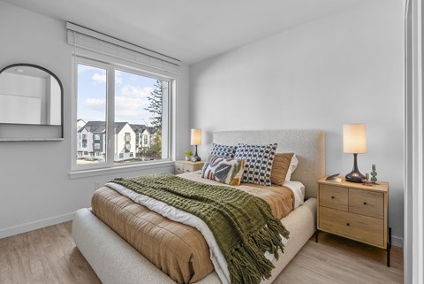 A bedroom with a bed, nightstand, and a window overlooking a residential area.