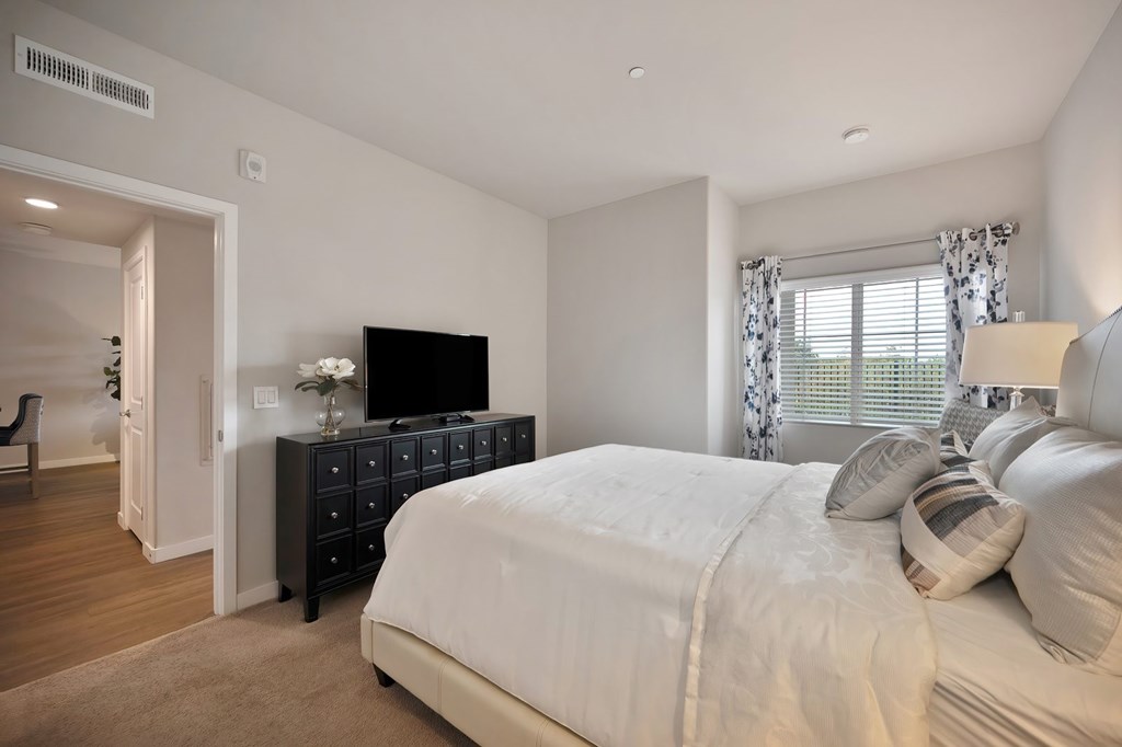 A bedroom with a large bed and a TV on a dresser.