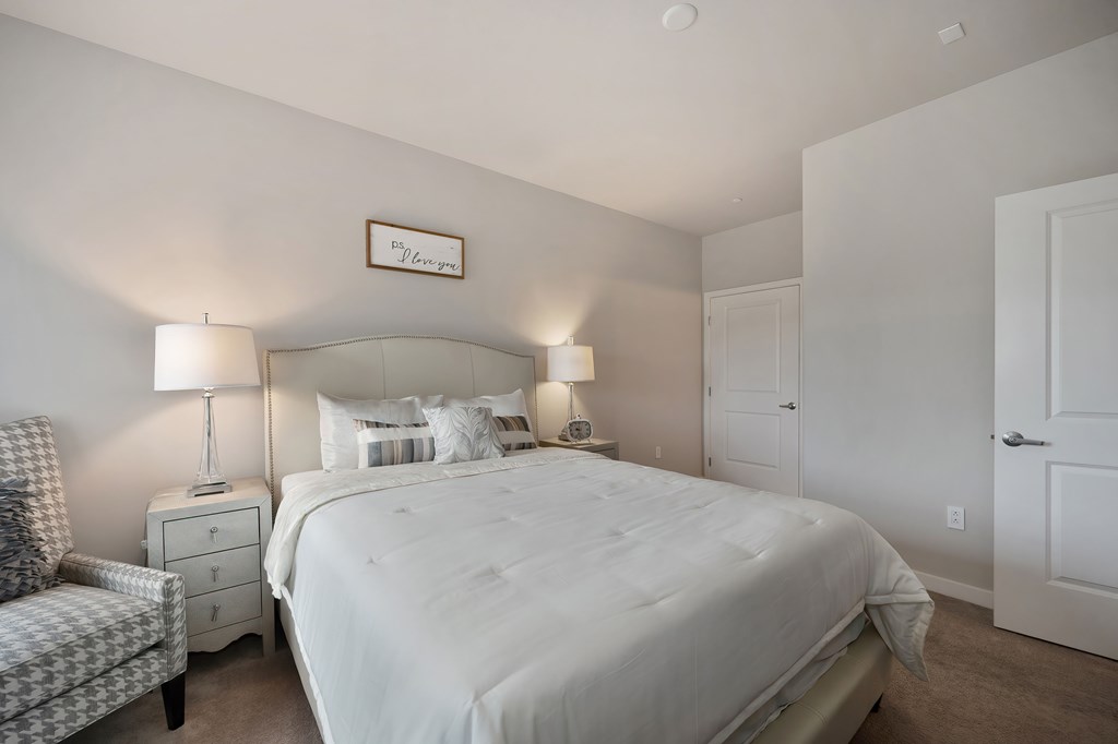 A bedroom with a large bed, a chair, and two lamps.