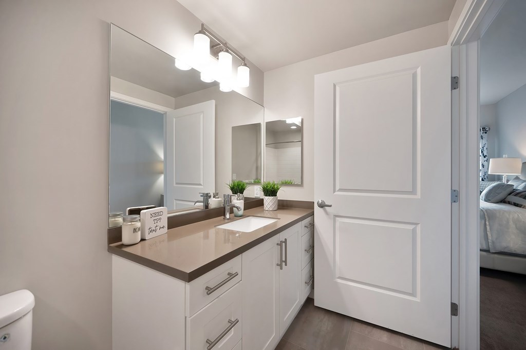 A bathroom with a white door and a mirror above the sink.