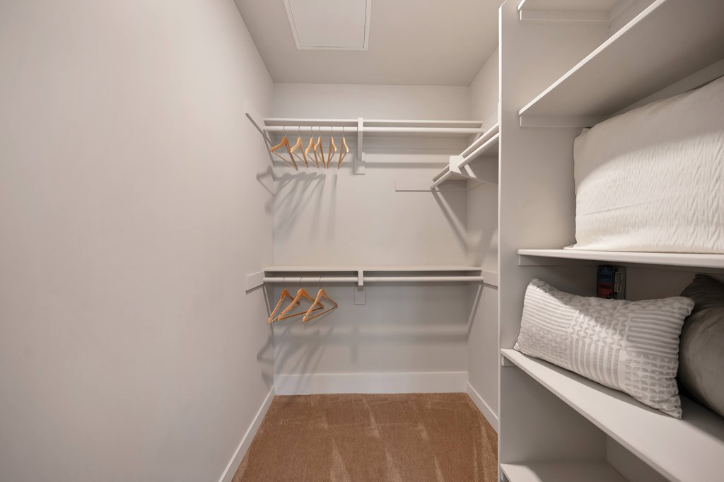 A walk-in closet with white shelves and hangers.