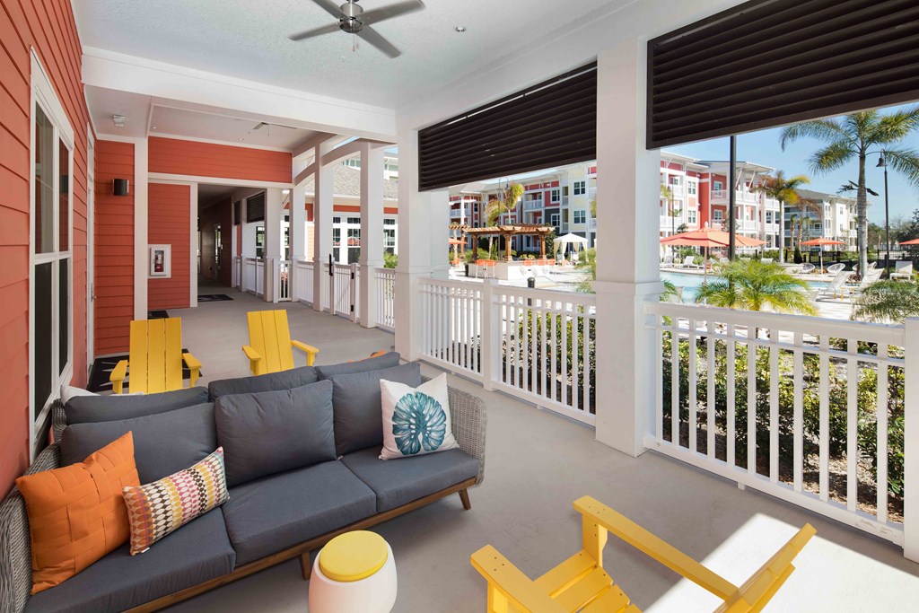 A balcony with a grey couch and yellow chairs overlooks a street.