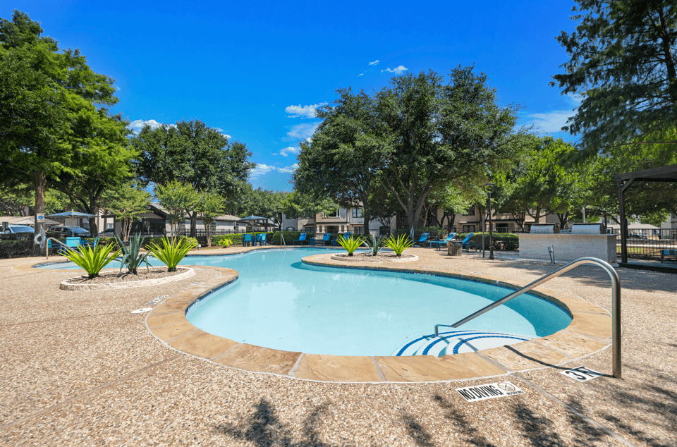 A large outdoor swimming pool surrounded by trees and plants.