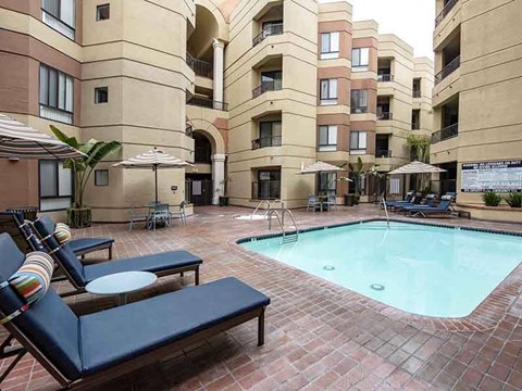 A pool surrounded by chairs and umbrellas in a courtyard.