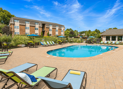 A pool surrounded by chairs and umbrellas with apartment buildings in the background.