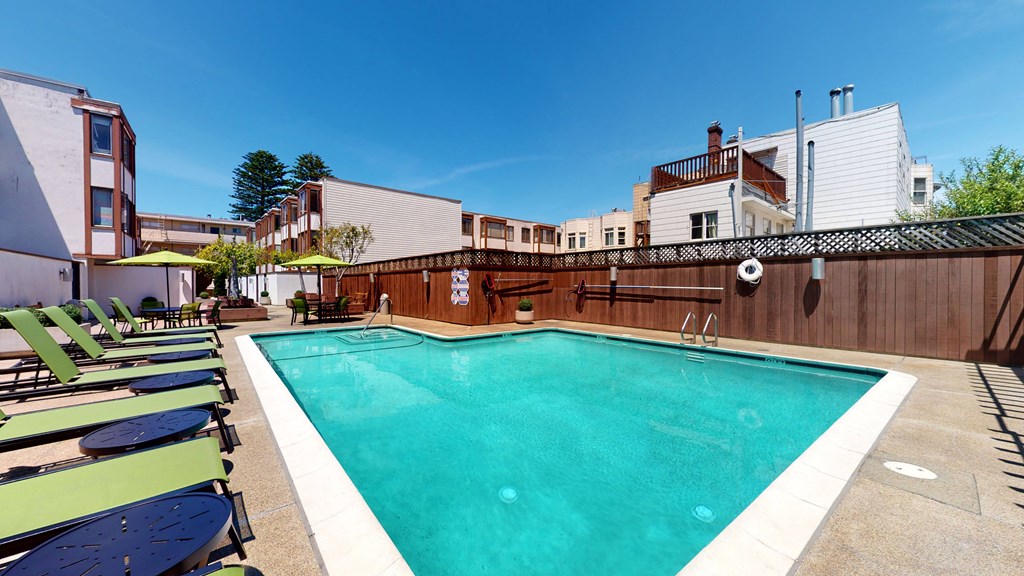 a swimming pool with chaise lounge chairs and umbrellas in front of a building