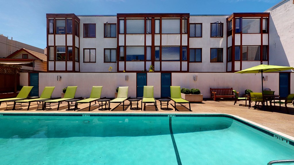 a swimming pool with green lounge chairs and a yellow umbrella in front of a white building