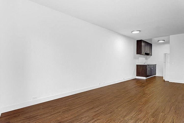an empty living room with a kitchen in the background