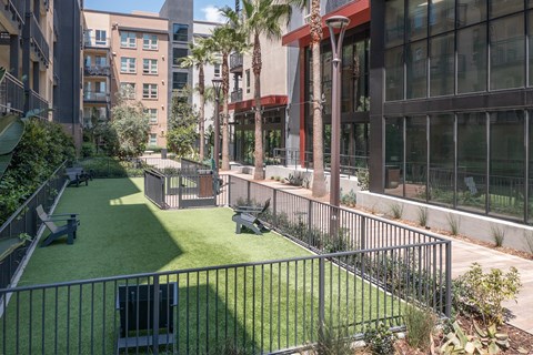 A green space with a fence and a bench is surrounded by buildings.