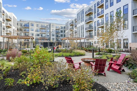 A courtyard with red chairs and plants in front of apartment buildings.