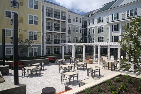 A patio with tables and chairs is surrounded by apartment buildings.