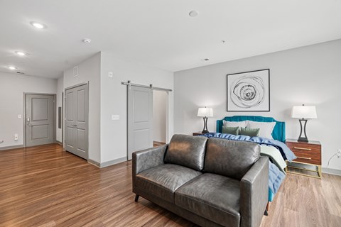 A modern bedroom with a leather couch and a bed with a blue blanket.
