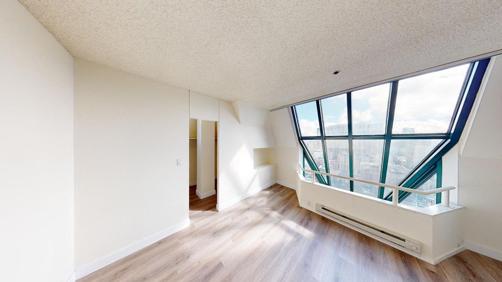 an empty apartment with a large window and hardwood floors