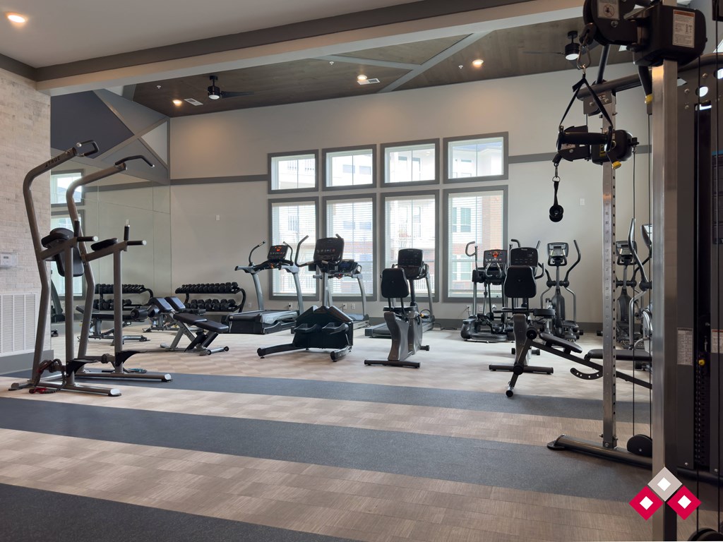 a spacious fitness room with weights and cardio equipment and windows