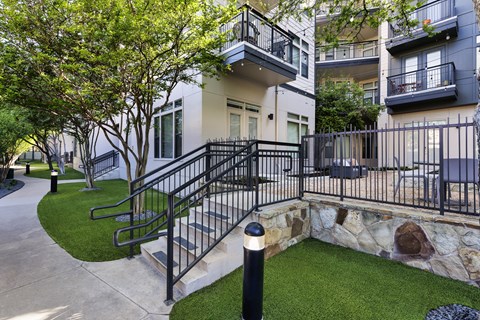 A black metal railing leads up to a stone wall and a green lawn.