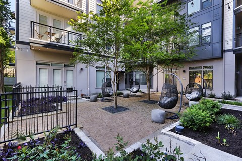 A small tree in a courtyard surrounded by hanging chairs.