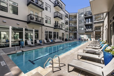 A large outdoor swimming pool with sun loungers and apartment buildings in the background.