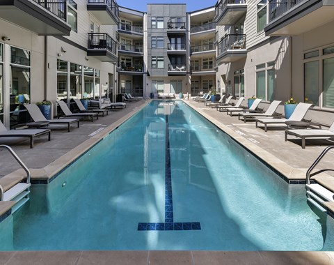 A long rectangular pool with a blue tiled border in the middle of a patio area.