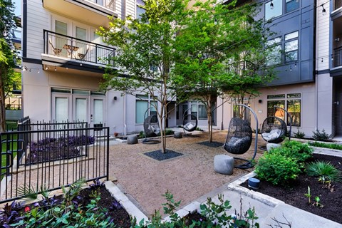 A small tree in a courtyard surrounded by hanging chairs and plants.