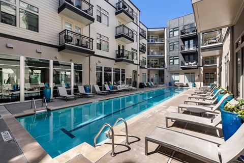 A swimming pool surrounded by lounge chairs and buildings.