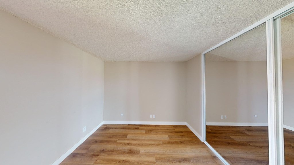 a bedroom with a large mirror and hardwood flooring