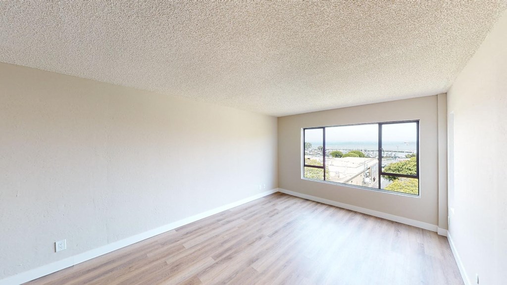 an empty bedroom with a large window and hardwood floors