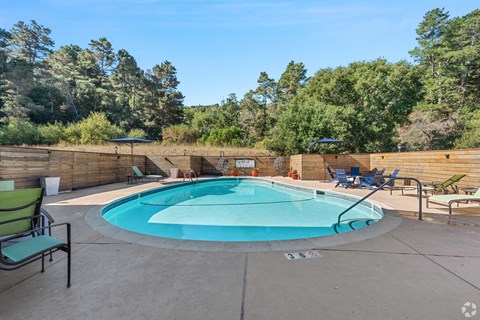 A round above ground pool with a concrete patio and a wooden fence.