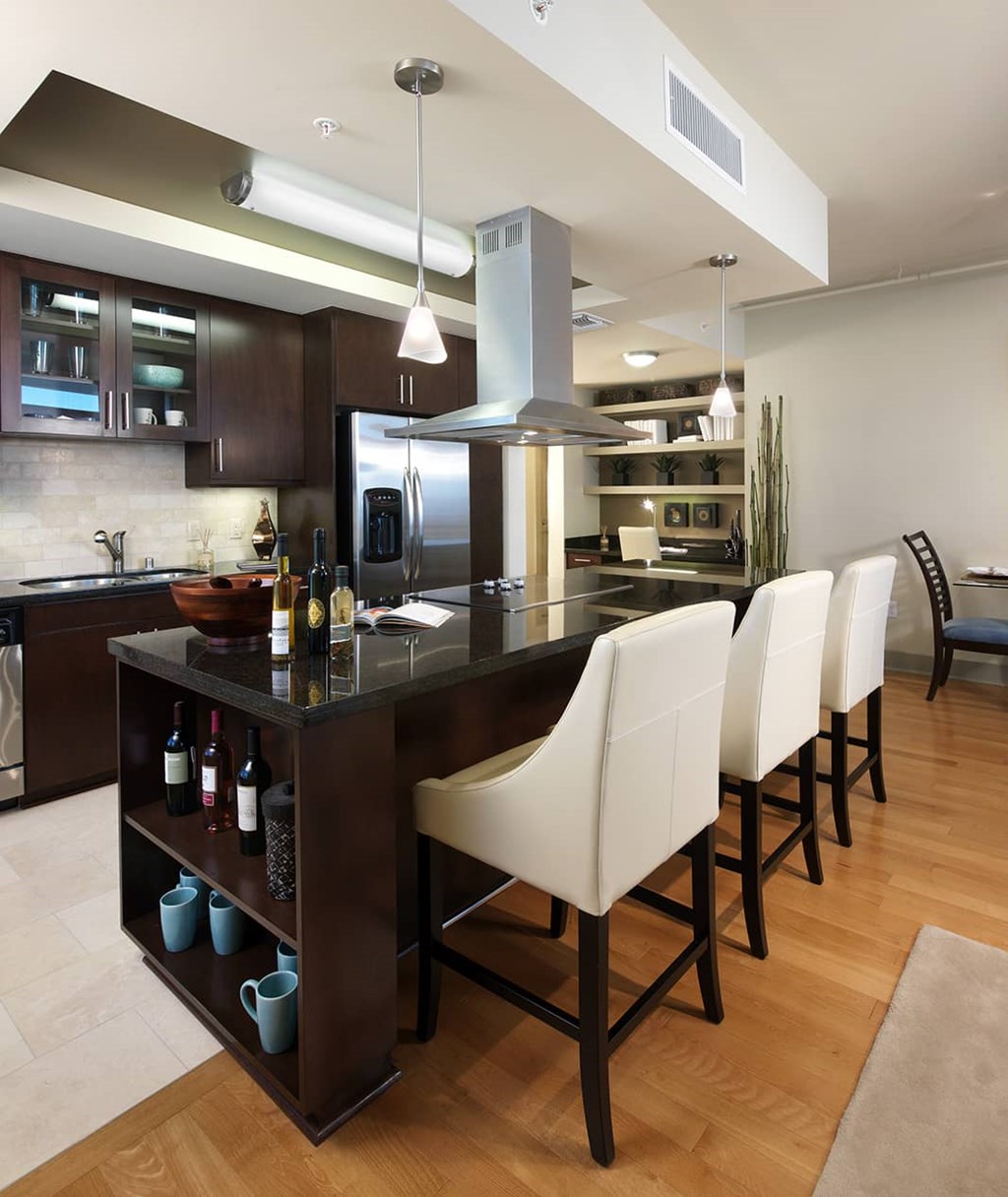 A modern kitchen with a dark wood island and white chairs.