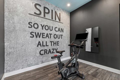 A spin bike in a room with a wall that says "SPIN SO YOU CAN SWEAT OUT ALL THE CRAZY".