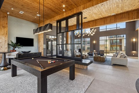 A billiard table is in the middle of a room with a glass wall and a couch.