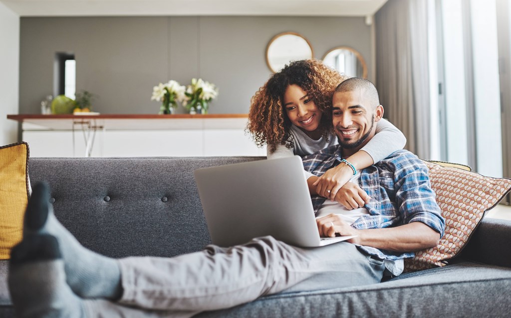 A man and woman are sitting on a couch with a laptop.