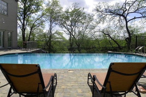 Two chairs are facing a pool with trees in the background.